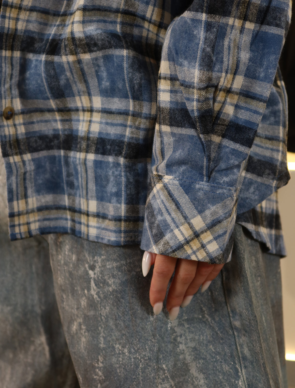 Close-up of a person wearing a blue, navy, and beige plaid flannel shirt with a distressed texture, paired with distressed gray jeans.